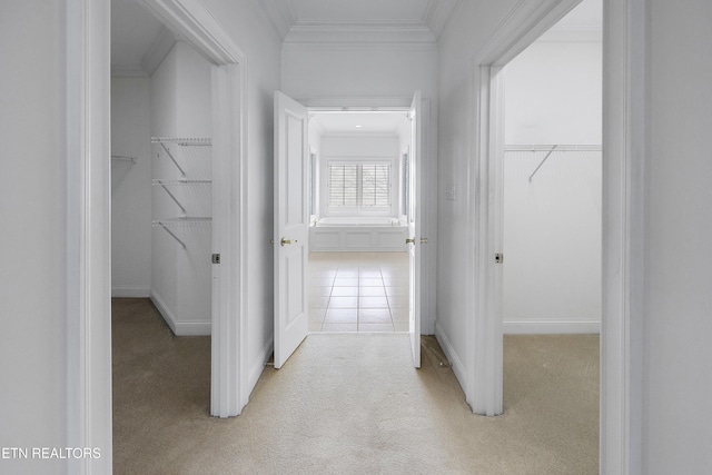 hall with ornamental molding, baseboards, and light colored carpet