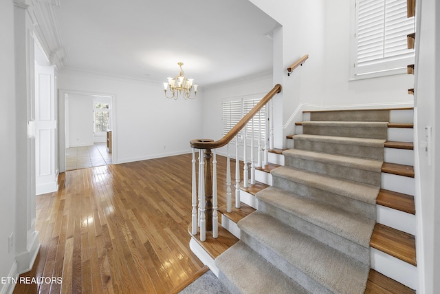 staircase with crown molding, baseboards, a notable chandelier, and wood finished floors