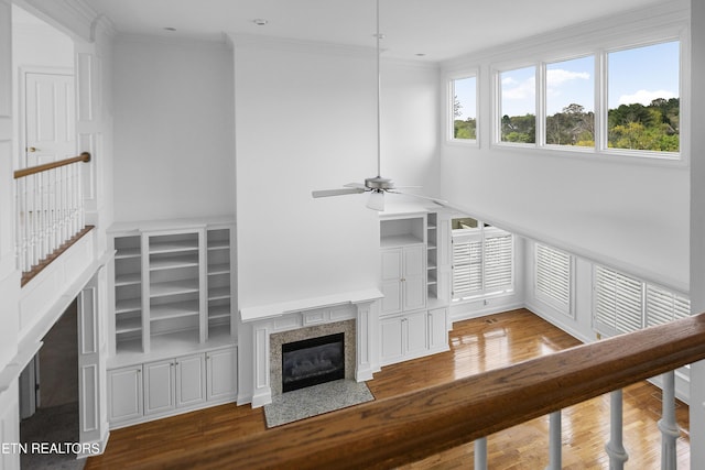 unfurnished living room featuring crown molding, a premium fireplace, ceiling fan, built in shelves, and wood finished floors