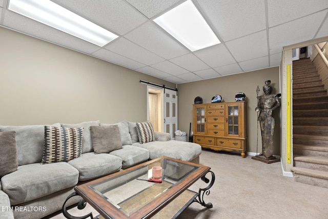 living room featuring a barn door, stairway, light colored carpet, and a drop ceiling