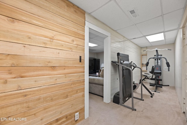 exercise room with a drop ceiling, carpet floors, and wooden walls