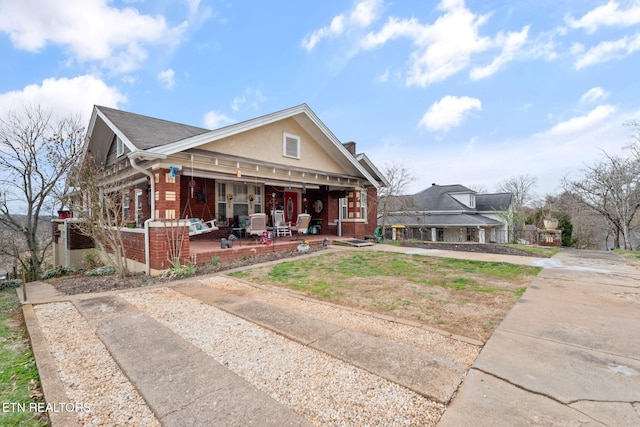 bungalow-style house with stucco siding, brick siding, and a porch