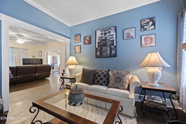 living room featuring wood finished floors, a textured ceiling, ornamental molding, and a ceiling fan