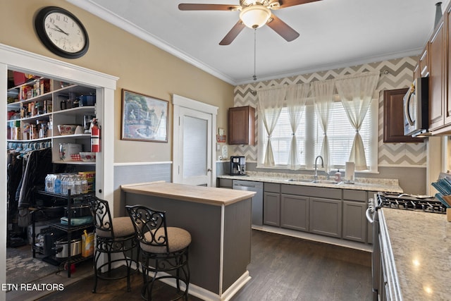 kitchen with dark wood-style flooring, ornamental molding, stainless steel appliances, light countertops, and a sink