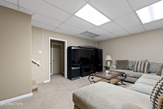 living room with baseboards, a drop ceiling, and light carpet