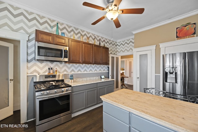 kitchen with wallpapered walls, dark wood finished floors, ornamental molding, light countertops, and appliances with stainless steel finishes