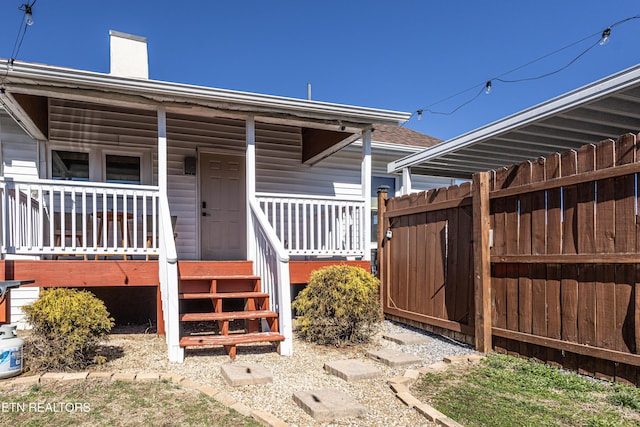 view of exterior entry with covered porch, a chimney, and fence