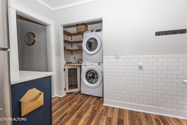 clothes washing area with stacked washer and clothes dryer, tile walls, wainscoting, laundry area, and dark wood-style flooring