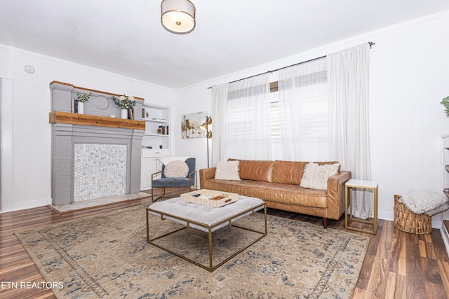 living area featuring a fireplace with flush hearth, wood finished floors, and crown molding