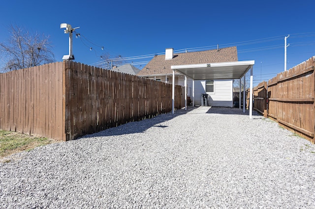 view of yard with gravel driveway, a carport, and a fenced backyard