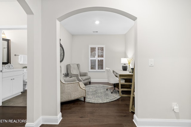 home office with dark wood-style floors, visible vents, arched walkways, and baseboards