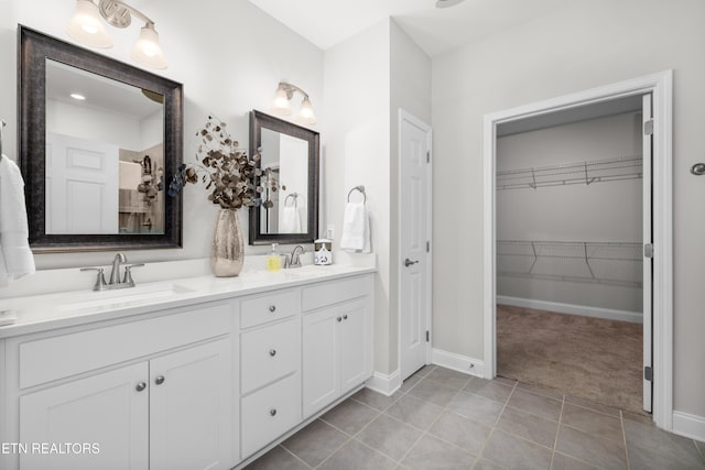 bathroom featuring tile patterned floors, double vanity, a walk in closet, and a sink