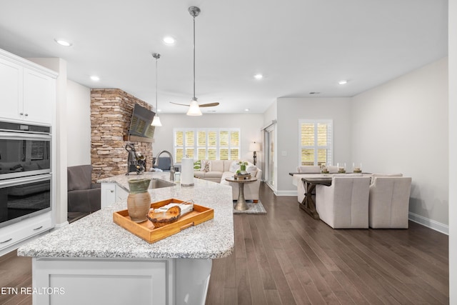 kitchen with dark wood finished floors, a sink, white cabinetry, double oven, and open floor plan