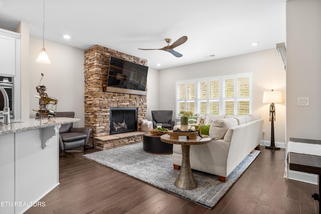 living area with baseboards, ceiling fan, dark wood finished floors, a stone fireplace, and recessed lighting