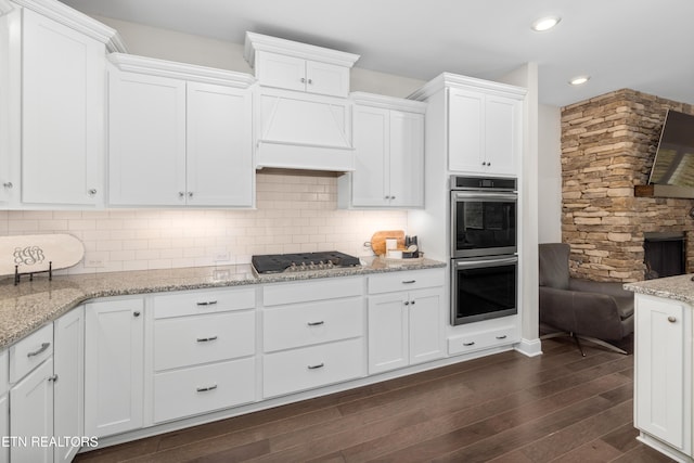 kitchen featuring dark wood finished floors, stainless steel appliances, decorative backsplash, custom range hood, and white cabinets