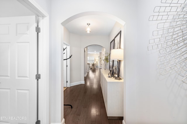 hall with arched walkways, dark wood-style flooring, and baseboards