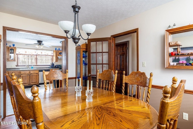 dining space with wood finished floors, ceiling fan with notable chandelier, and a textured ceiling