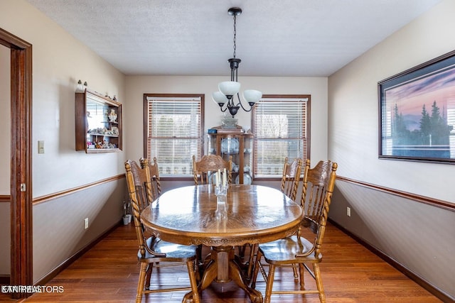 dining space with wood finished floors, baseboards, a chandelier, and a textured ceiling