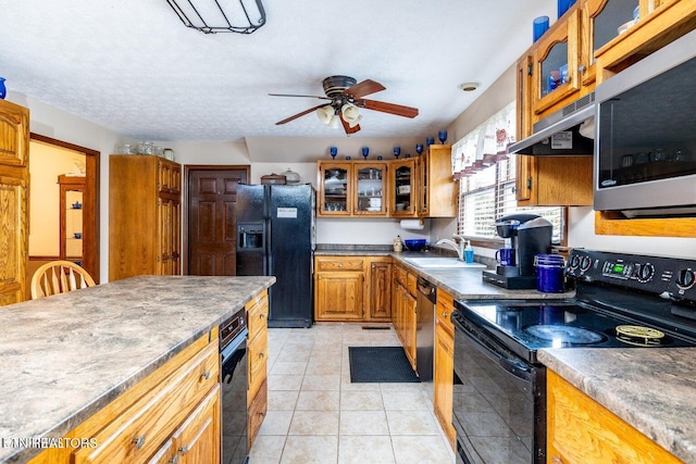 kitchen with light tile patterned flooring, a sink, black appliances, under cabinet range hood, and brown cabinets