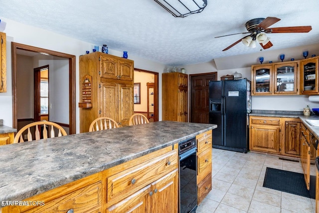 kitchen featuring dark countertops, glass insert cabinets, light tile patterned floors, black fridge, and brown cabinetry