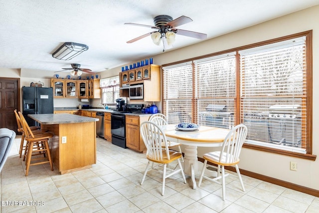 kitchen featuring a center island, glass insert cabinets, baseboards, brown cabinets, and black appliances