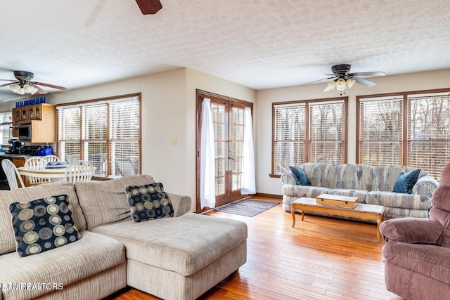 living room with hardwood / wood-style floors, ceiling fan, baseboards, and a textured ceiling