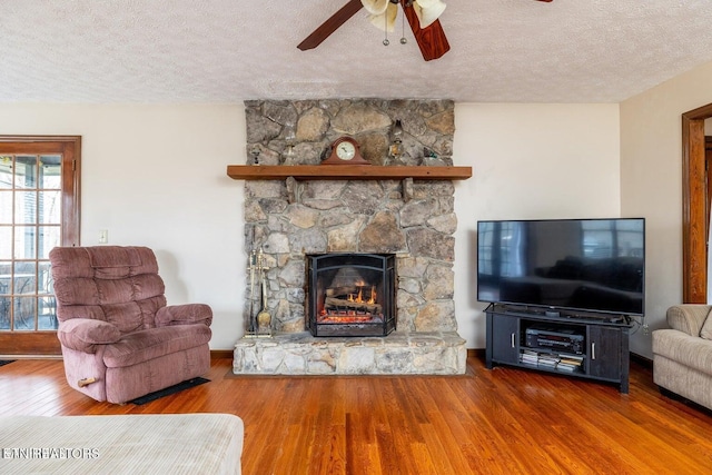 living room featuring baseboards, a fireplace, wood finished floors, a textured ceiling, and a ceiling fan