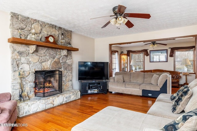 living area with a wealth of natural light, a fireplace, a textured ceiling, and wood finished floors