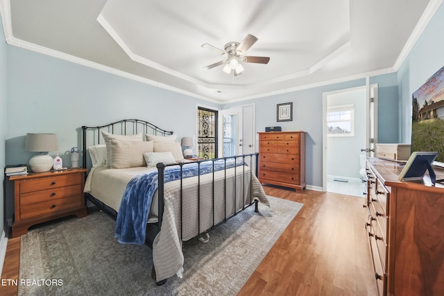 bedroom with light wood-type flooring, a tray ceiling, baseboards, and crown molding