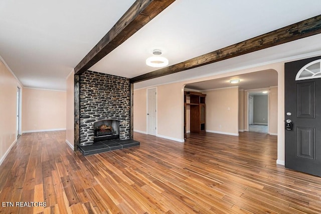 unfurnished living room with beamed ceiling, arched walkways, wood finished floors, and a tiled fireplace