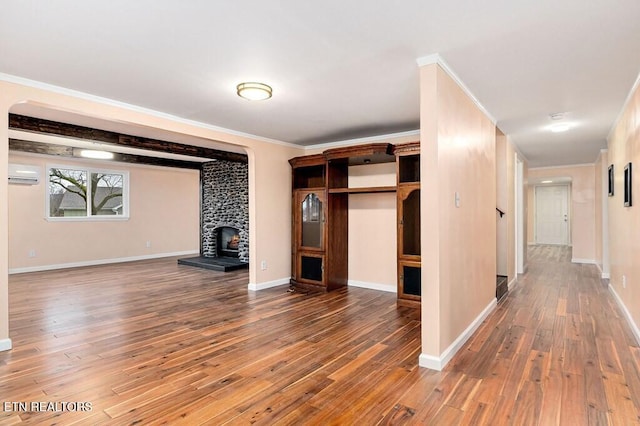 unfurnished living room with a wall mounted air conditioner, ornamental molding, hardwood / wood-style floors, a fireplace, and baseboards