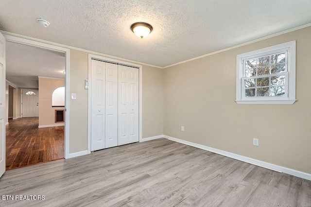 unfurnished bedroom with wood finished floors, baseboards, a closet, a textured ceiling, and crown molding