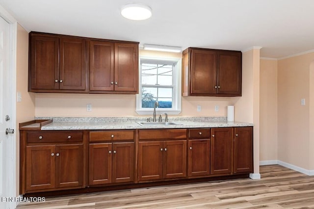 kitchen with crown molding, baseboards, light stone countertops, light wood-type flooring, and a sink