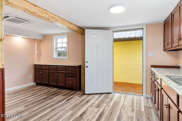 kitchen featuring light wood-type flooring, visible vents, beam ceiling, light countertops, and baseboards