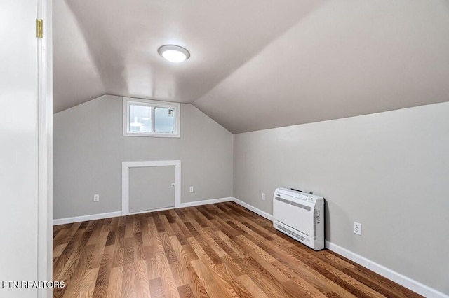 additional living space with vaulted ceiling, heating unit, wood finished floors, and baseboards