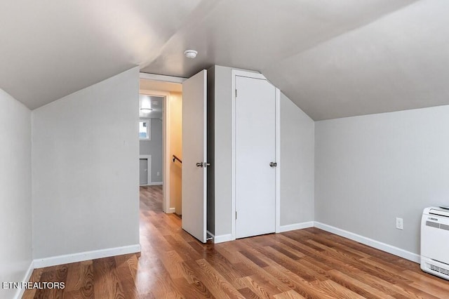 additional living space featuring lofted ceiling, heating unit, wood finished floors, and baseboards