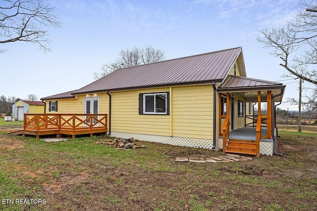 rear view of property with a wooden deck, a porch, an outdoor structure, a storage unit, and metal roof