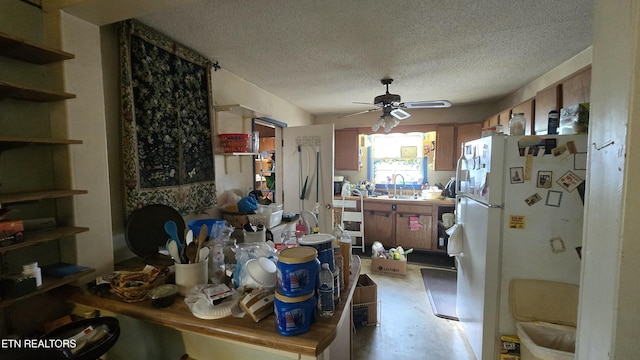 kitchen featuring a ceiling fan, concrete floors, freestanding refrigerator, a sink, and a textured ceiling