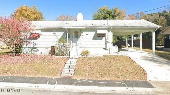 view of front facade with an attached carport, concrete driveway, crawl space, and a chimney