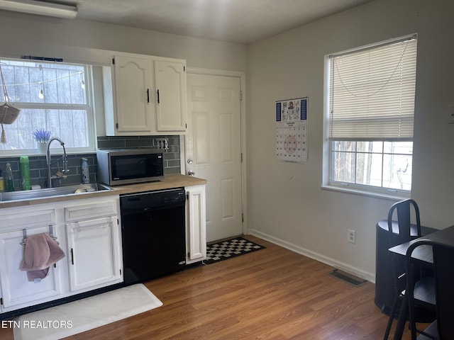 kitchen featuring a sink, stainless steel microwave, black dishwasher, white cabinetry, and decorative backsplash