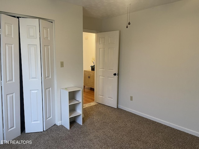 unfurnished bedroom featuring a closet, baseboards, and dark carpet