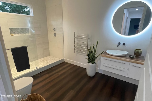 bathroom with a walk in shower, wood finished floors, radiator, baseboards, and vanity