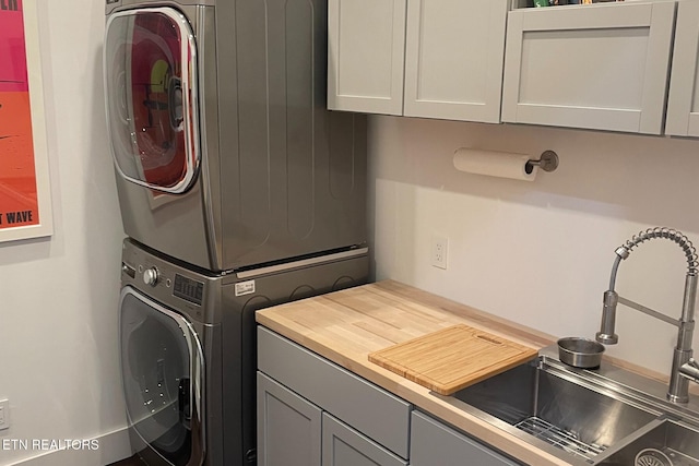 laundry area featuring a sink, stacked washer / drying machine, and cabinet space