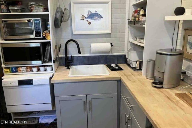 kitchen featuring a sink, stainless steel microwave, open shelves, and gray cabinetry