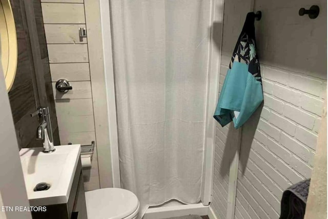 bathroom featuring a shower with shower curtain, toilet, brick wall, and vanity