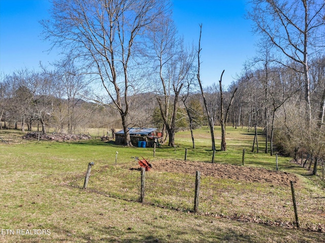 view of yard featuring a rural view, a forest view, fence, a shed, and an outbuilding