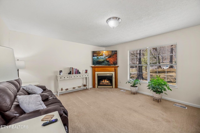 carpeted living room with baseboards, visible vents, a warm lit fireplace, and a textured ceiling