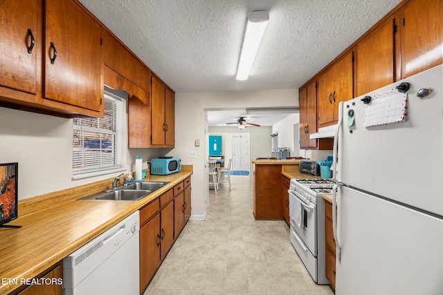 kitchen featuring white appliances, a sink, light countertops, under cabinet range hood, and brown cabinets