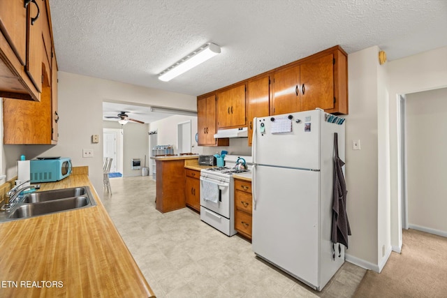 kitchen with white appliances, brown cabinetry, a sink, light countertops, and under cabinet range hood