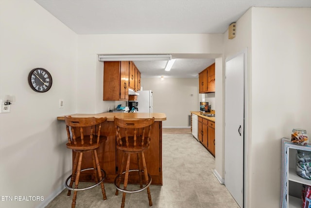 kitchen with freestanding refrigerator, a peninsula, a breakfast bar area, brown cabinetry, and light countertops